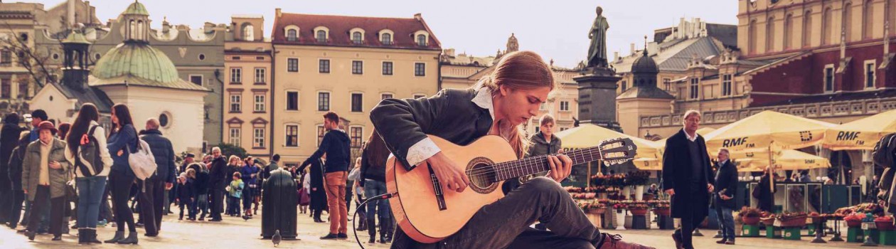Dekoratives Bild: Ein junger Mann sitz auf einem Marktplatz und spielt Gitarre.